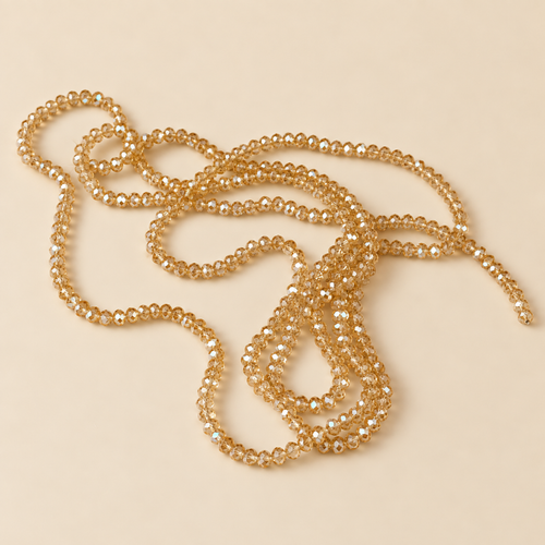 A long strand of small, faceted gold beads draped in loose loops on a solid, warm beige background.