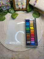 A set of pastel drawing sheets and a matching 5-color pastel pencil tray arranged on a woven round mat. The clear plastic sheet has a white circular mark, and the pencil tray contains pastel sticks in blue, green, yellow, orange, brown, pink, purple, and blue.